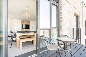 Un apartamento moderno con balcón, un comedor con mesa y sillas de madera, y un televisor montado en la pared.