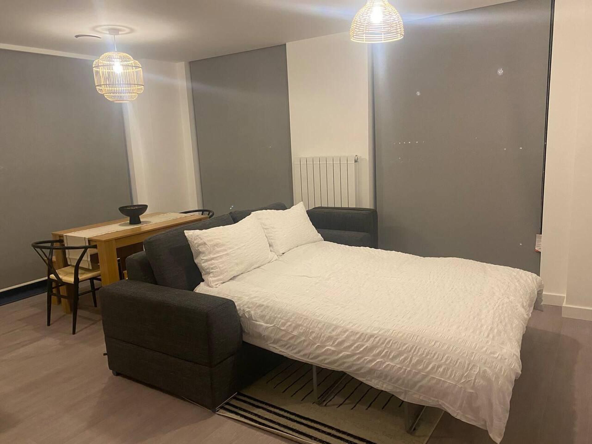 A modern bedroom with a bed, a desk, and two pendant lights.