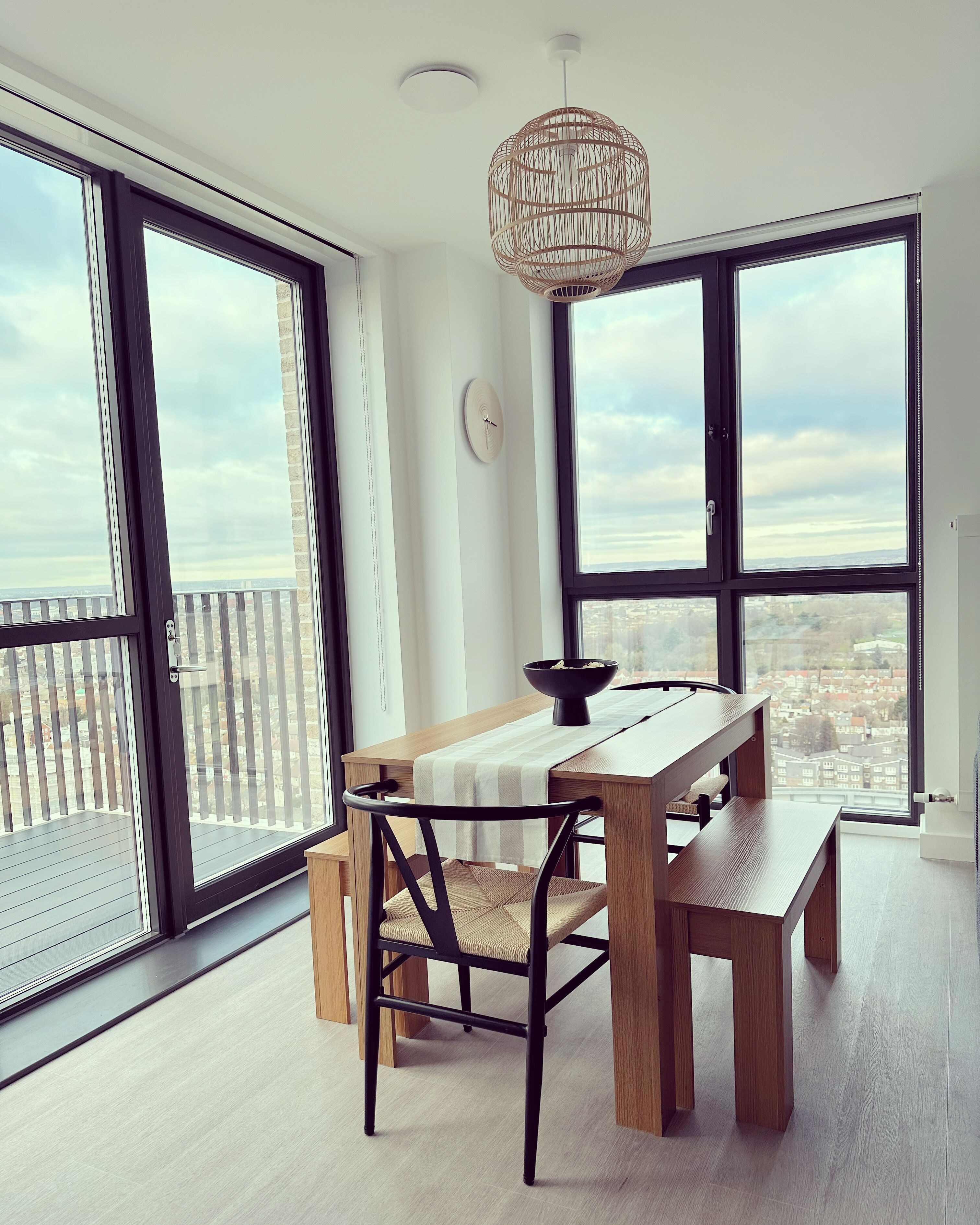 A modern dining area with a wooden table and chairs, large windows with city views, and a unique woven light fixture.