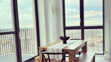 A modern dining area with a wooden table and chairs, large windows with city views, and a unique woven light fixture.