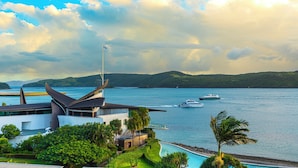 A modern hotel with a pool, a view of the sea, and a boat in the distance.