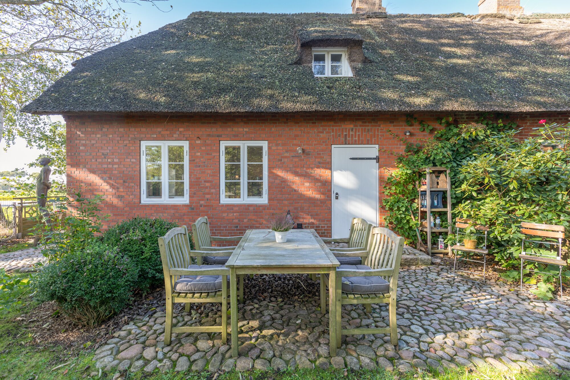 A brick house with a thatched roof, a stone patio, and a wooden table with chairs.