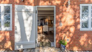 Un bâtiment en briques avec une porte blanche donne sur un espace repas comprenant une table et des chaises.