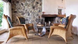 Una habitación con sillas de mimbre, pared de piedra, chimenea y una mesa con superficie de vidrio.