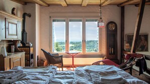 Un dormitorio con una cama grande, un aparador de madera, una silla, una mesa y vistas al exterior a través de tres ventanas.