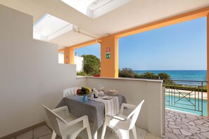 A balcony with a table set for breakfast, a view of the sea, and a clear sky.