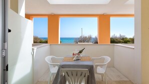Un balcón con mesa y sillas, una botella y vista al mar.