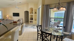 Una cocina moderna con comedor, que incluye una mesa y sillas de vidrio, un ventilador de techo y vistas al exterior.