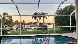 Una piscina con agua cristalina, rodeada por una cerca blanca, y vistas a una zona residencial con casas y palmeras.