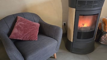 A room with a grey armchair, a wood-burning stove, and a bag of wood.
