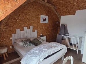 Un dormitorio con techo inclinado, cama con ropa de cama blanca, mesita de noche, cuna y pared de madera.