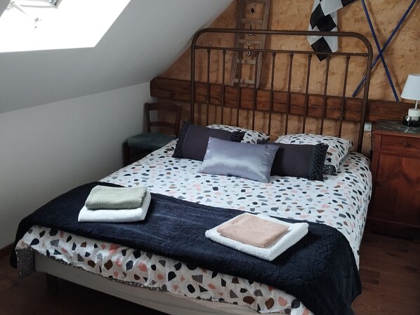 A bedroom with a sloped ceiling, a bed with patterned bedding, a bedside table, and a nightstand.