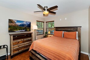 A bedroom with a bed, a ceiling fan, a dresser, a window with blinds, and a painting on the wall.
