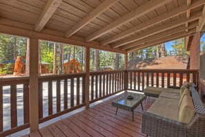 A covered outdoor deck with wooden railings, a glass-top table, and a wicker sofa.