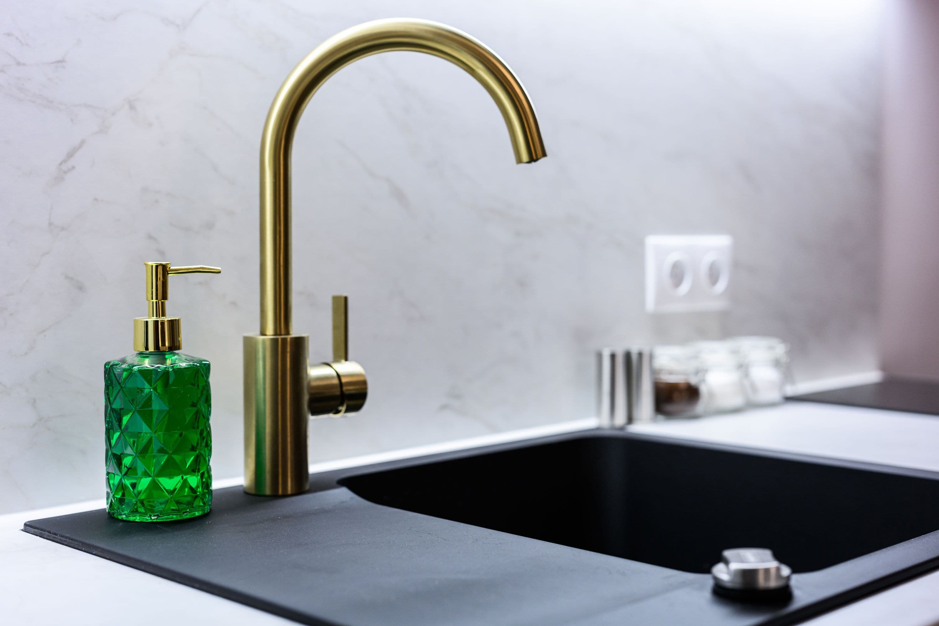 A modern kitchen with a black countertop, a gold faucet, and a green bottle.