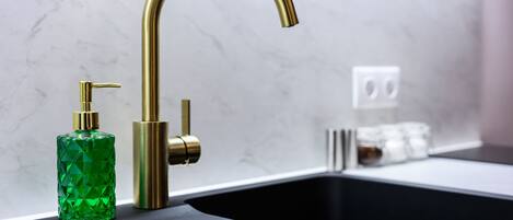 A modern kitchen with a black countertop, a gold faucet, and a green bottle.