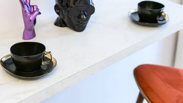 A modern kitchen with a white countertop, two red bar stools, a black coffee cup, a purple hand figurine, and a black pot with a plant.