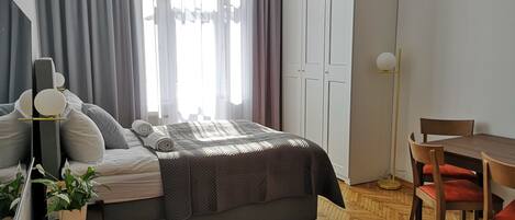 Un dormitorio moderno con cama, mesita de noche, lámpara y un comedor con sillas y una mesa.