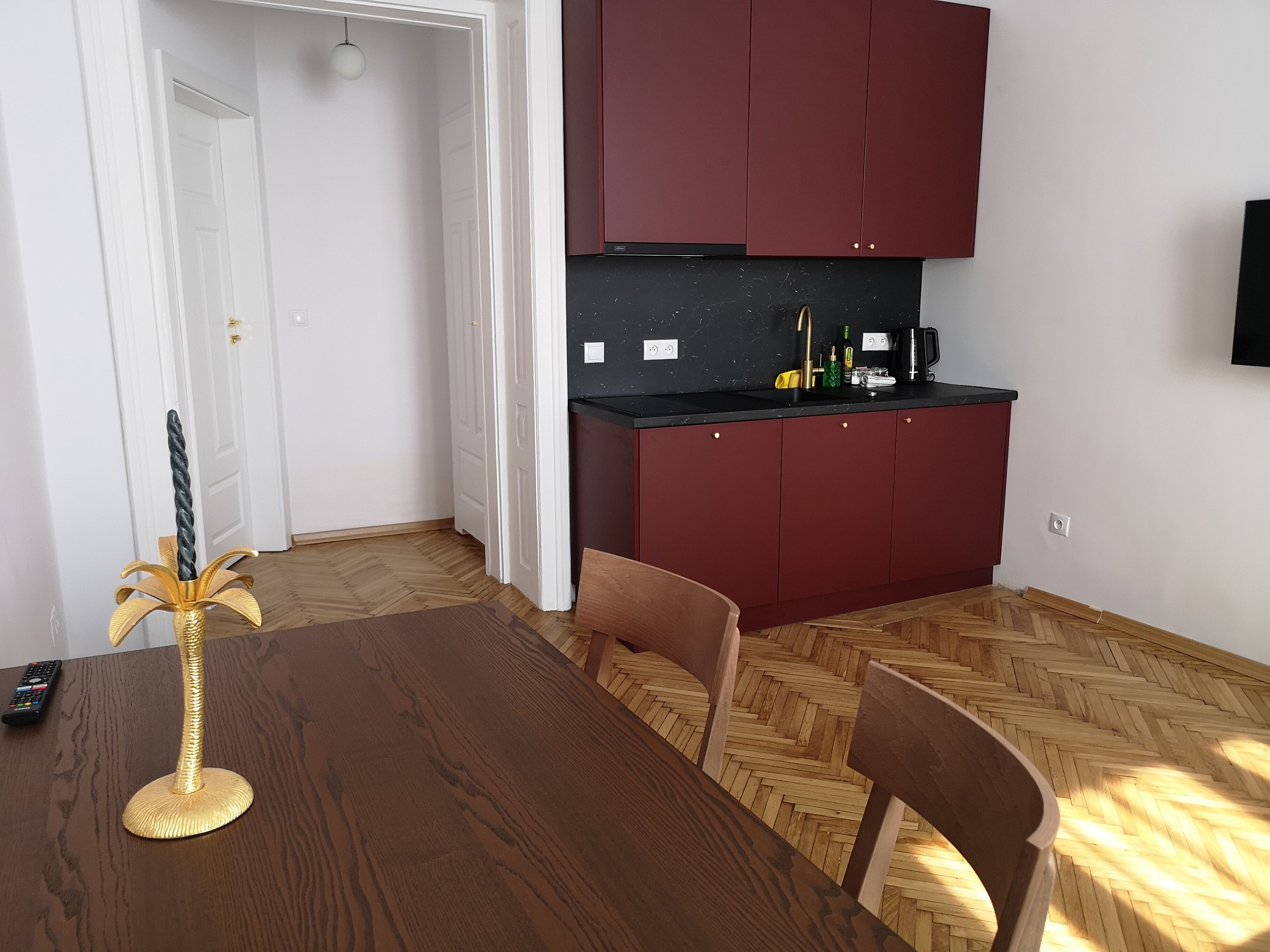 A dining area with a wooden table and chairs, a decorative golden object, and a kitchen with red cabinets and a black countertop.