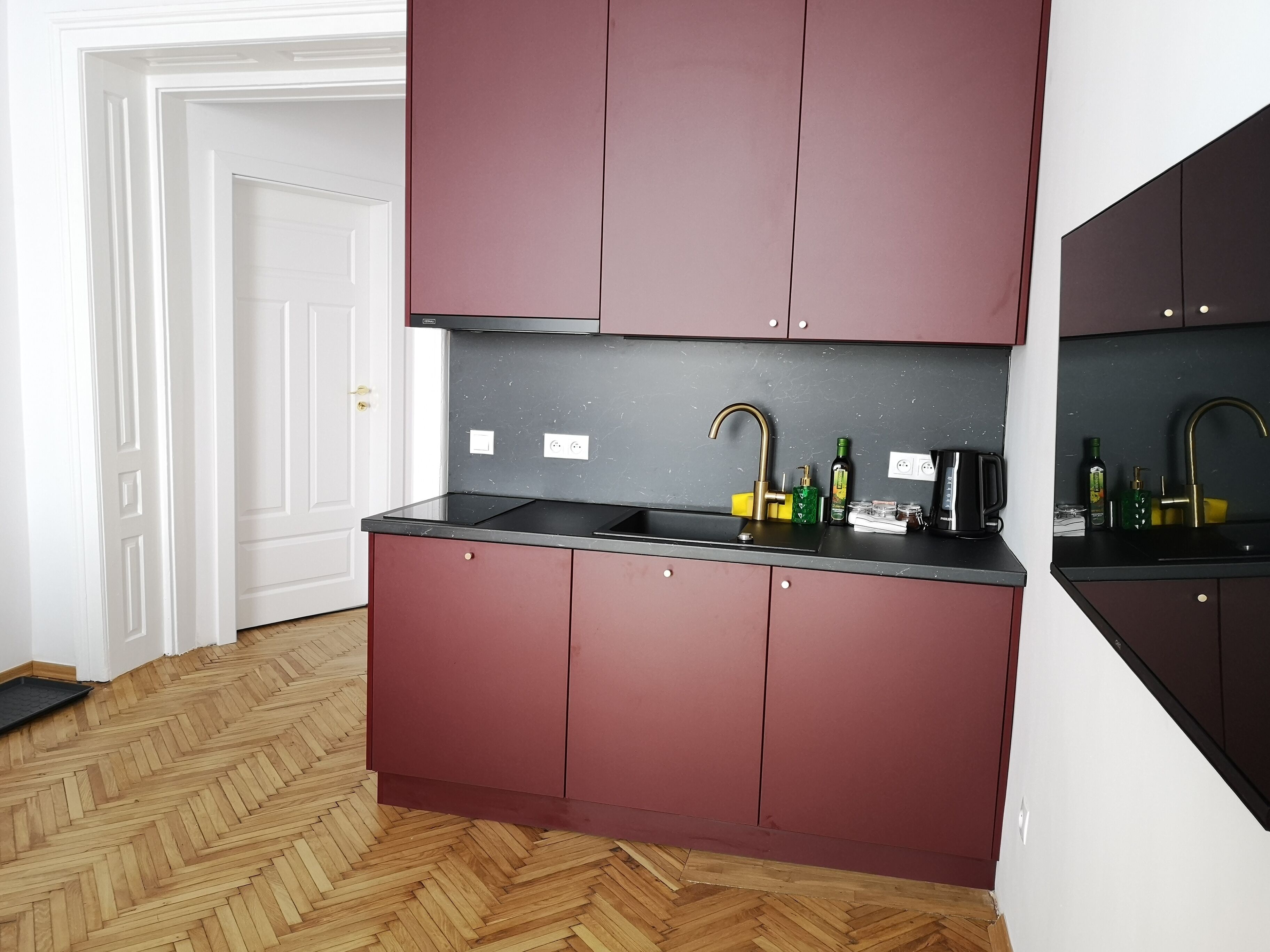 A modern kitchen with dark cabinets, a black countertop, and a herringbone wood floor.