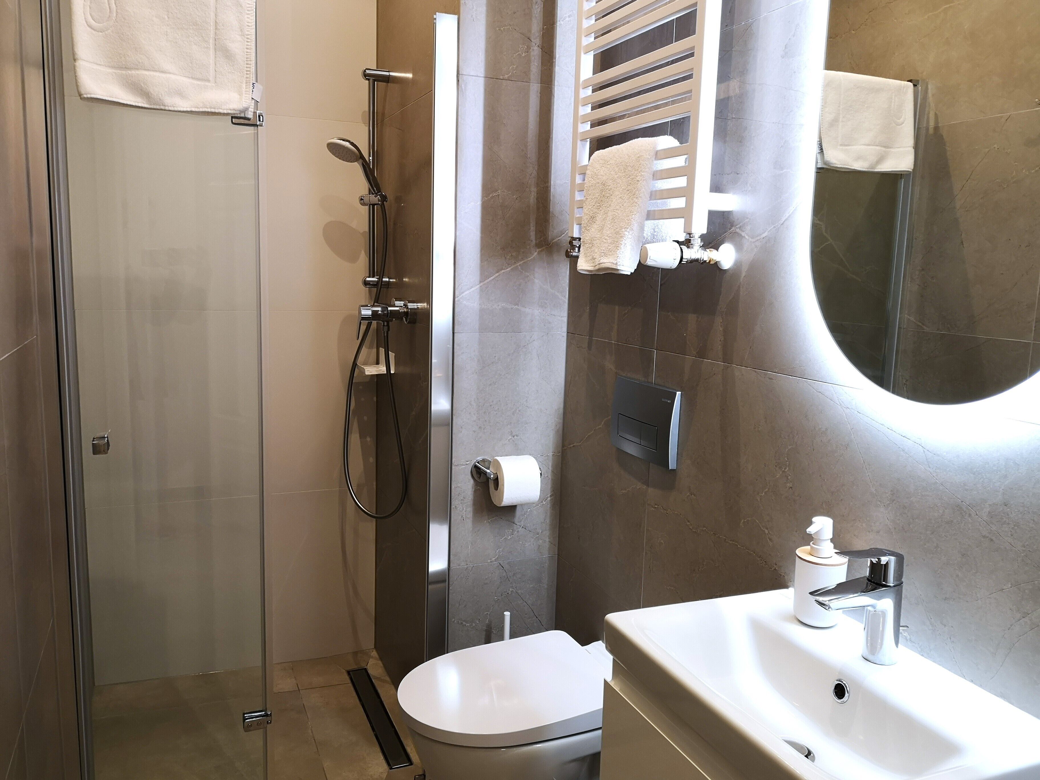 Un bany modern amb dutxa de vidre, un vàter blanc i un lavabo amb mirall.