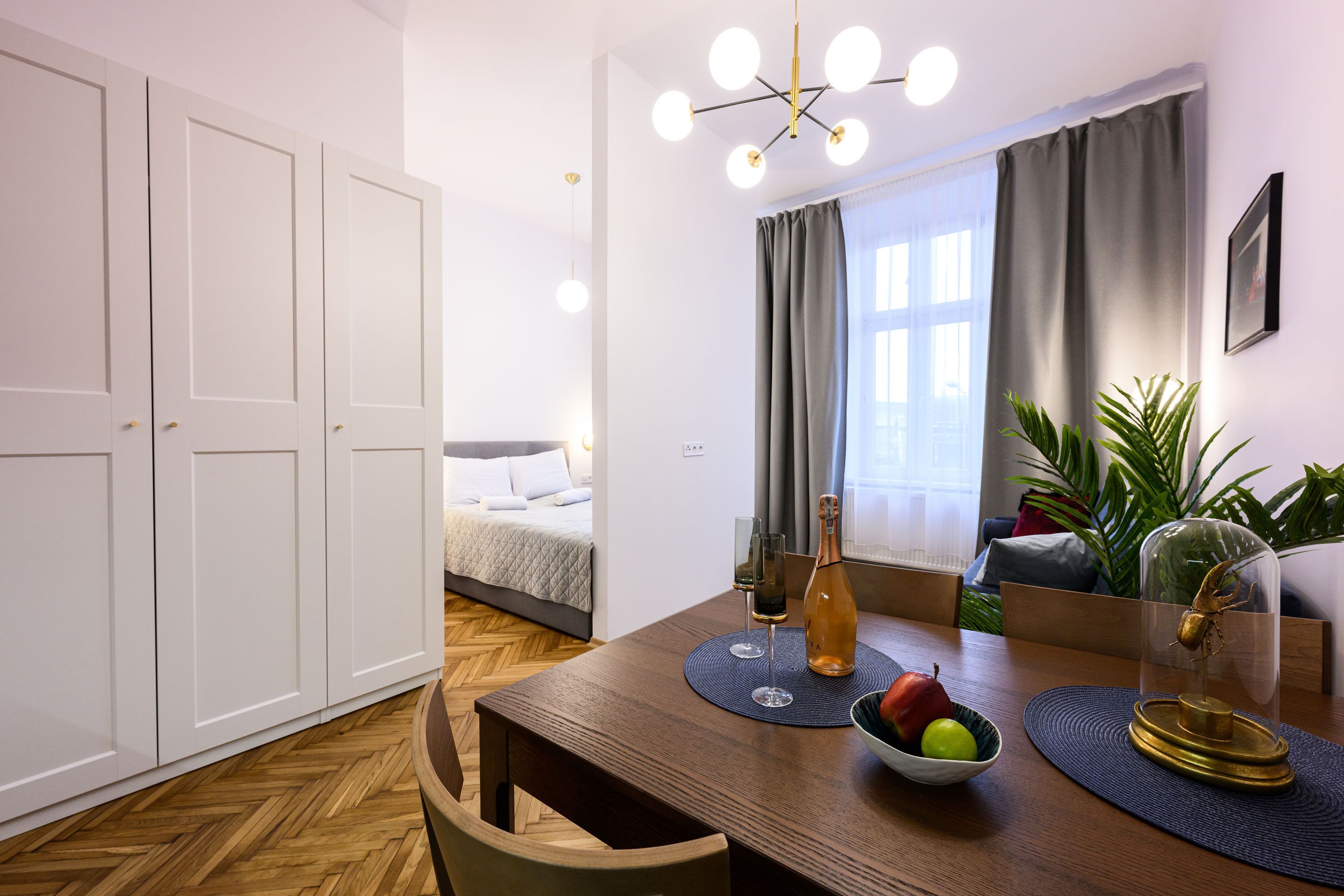 A modern room with a wooden dining table, a bed, and a large window with curtains.