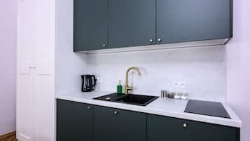 A kitchen with a black sink, a green soap dispenser, and a coffee maker.