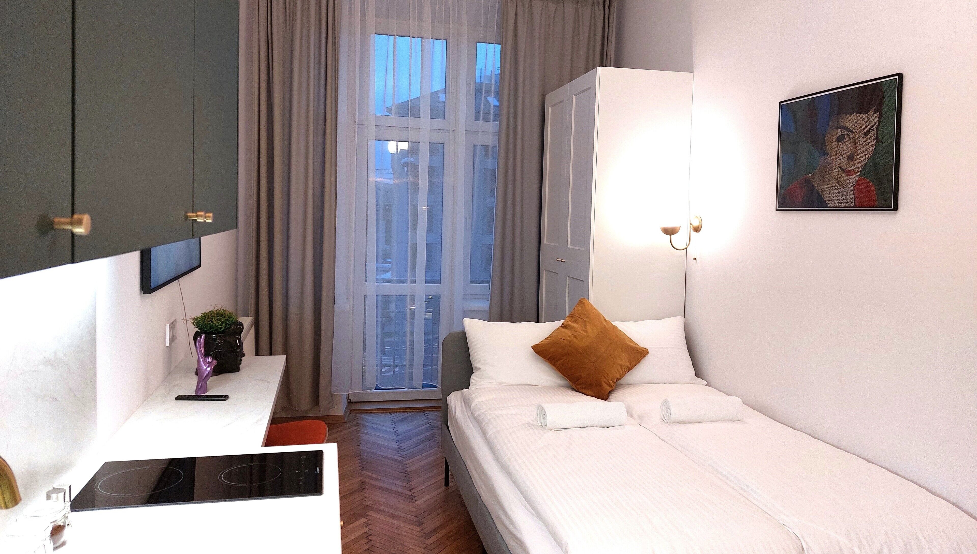 Ein modernes Hotelzimmer mit Bett, Schreibtisch, Flachbildfernseher und einem fensterbelaubten Fenster.
