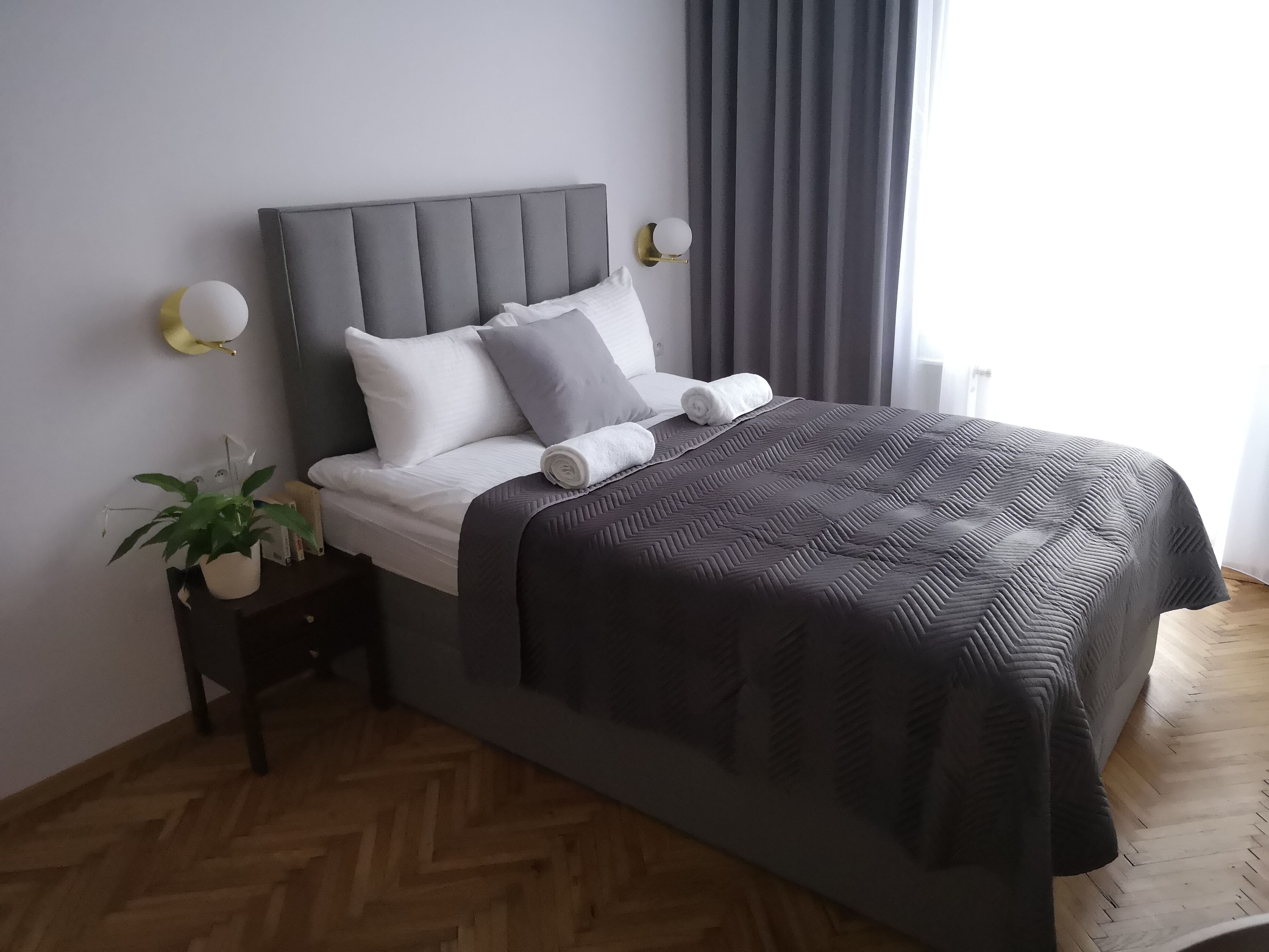 A modern bedroom with a grey upholstered headboard, white bedding, and a dark grey quilted bedspread.