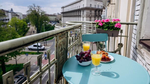 En balkon med et bord dækket til to personer, med en skål druer, et glas appelsinjuice og en croissant.
