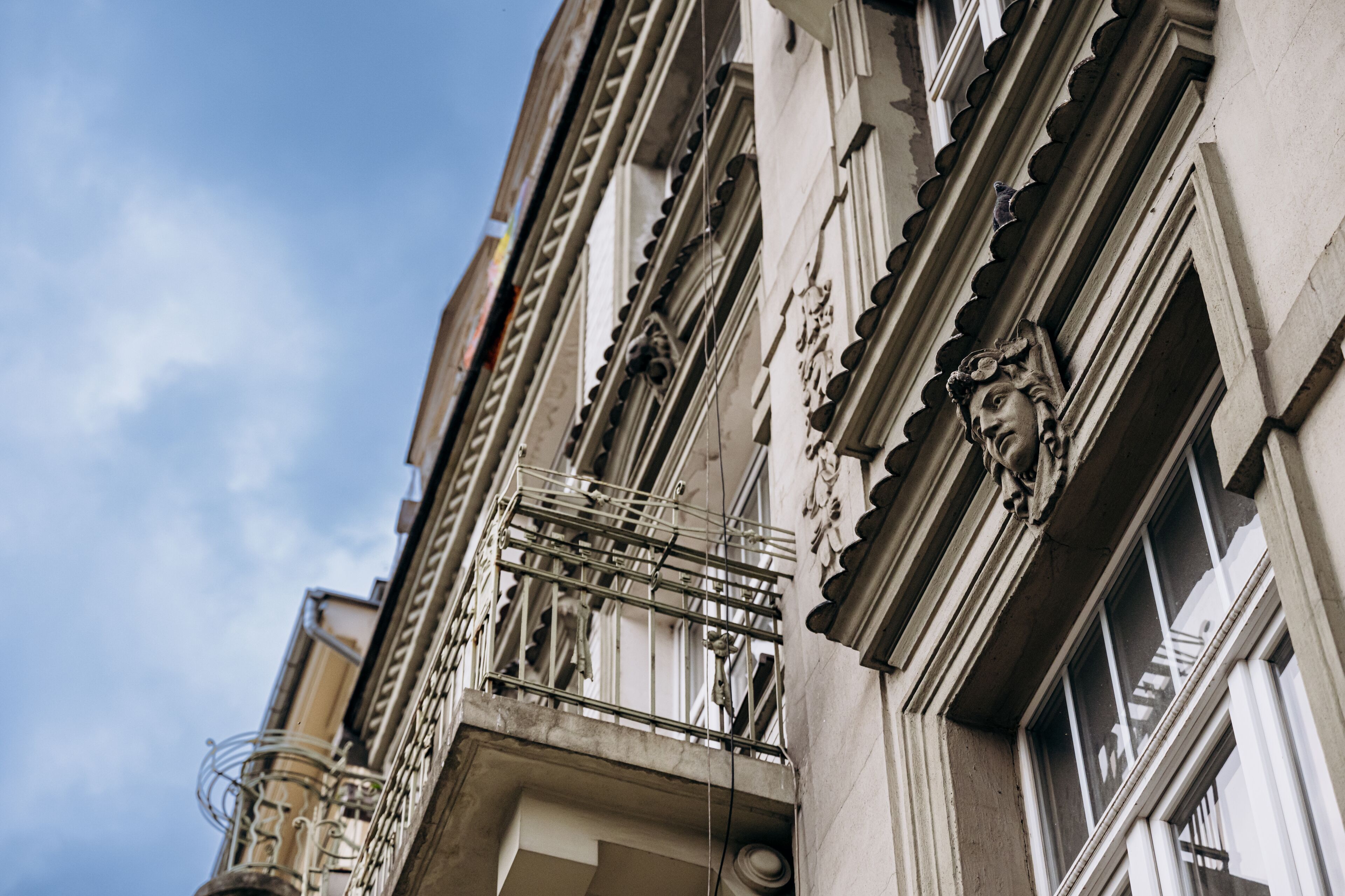 A multi-story building with ornate architectural details, including decorative moldings and a balcony with metal railings.
