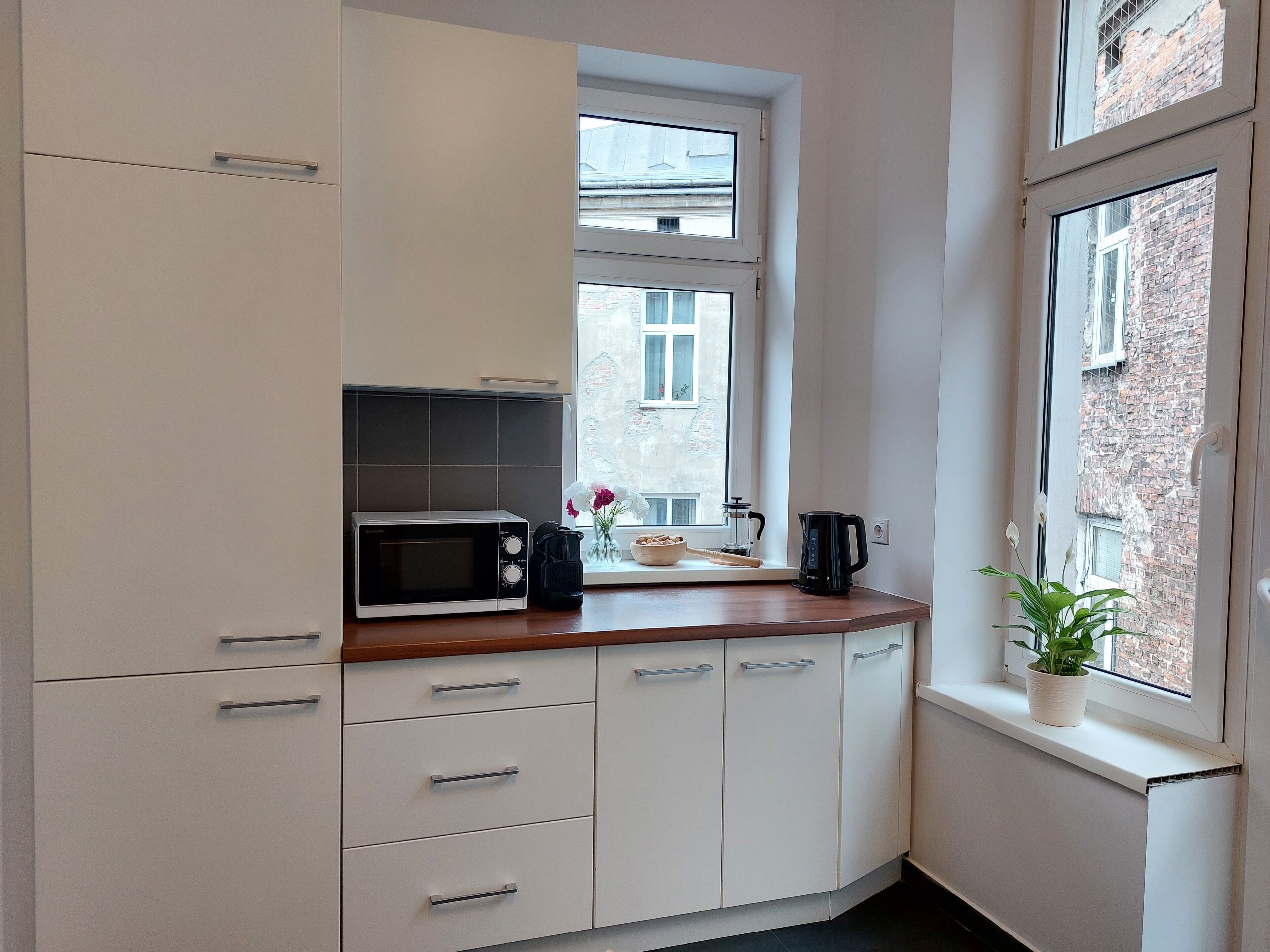 A kitchen with white cabinets, a microwave, a coffee maker, and a window with a view of a brick building.