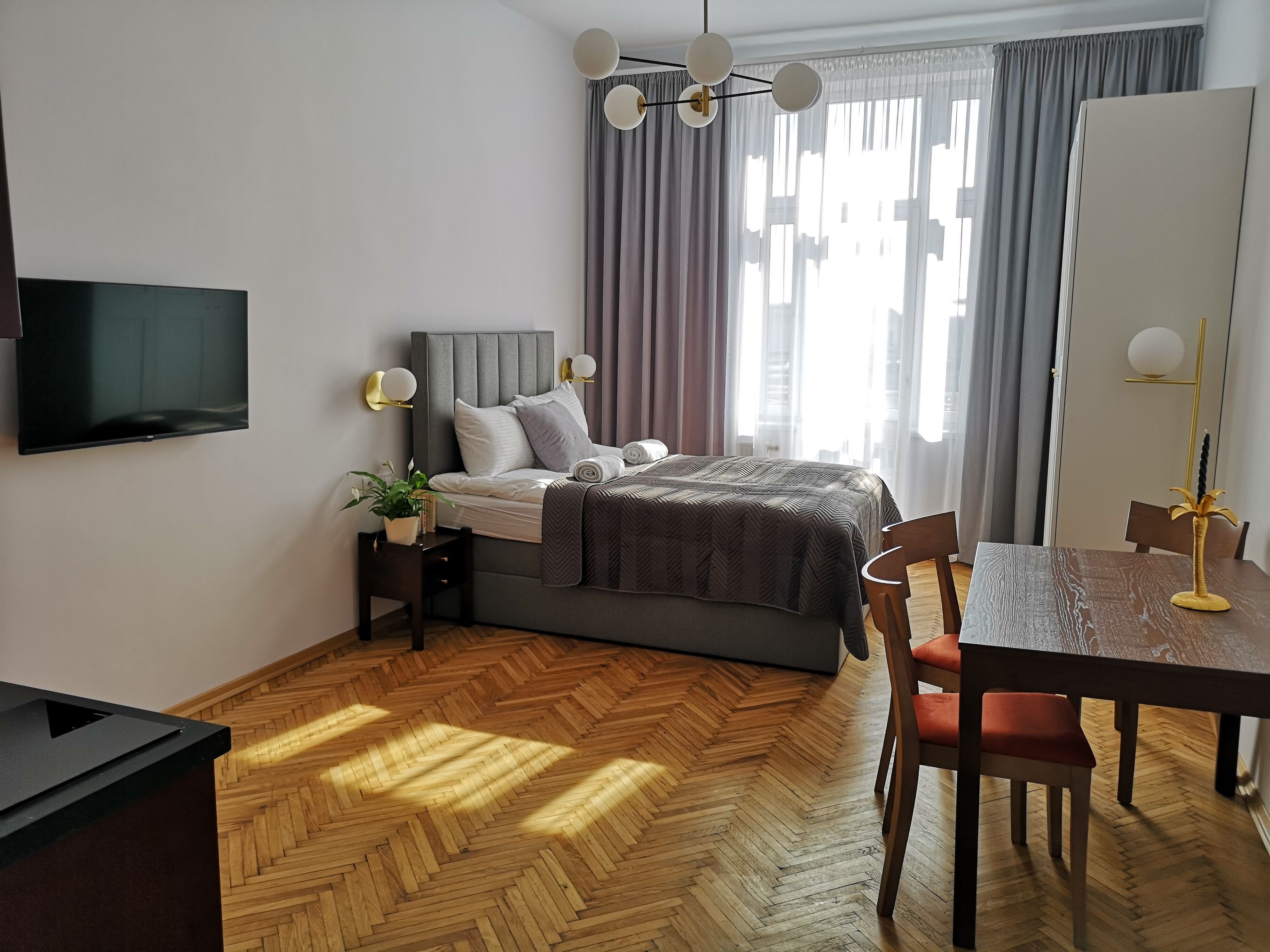 A modern hotel room with a bed, a desk, a chair, a television, and a dining table.
