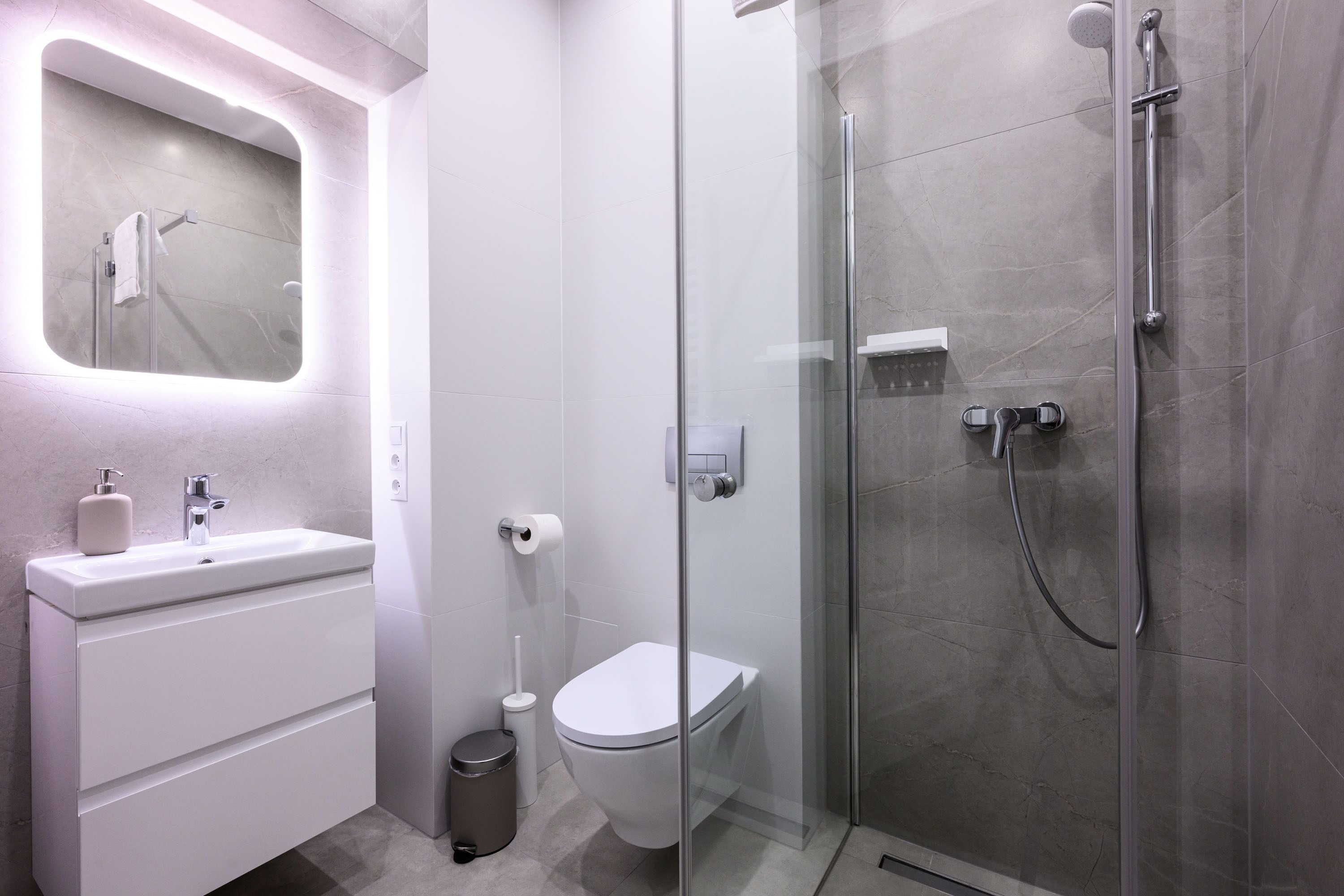 A modern bathroom with a glass-enclosed shower, a white sink with a mirror, and a toilet.