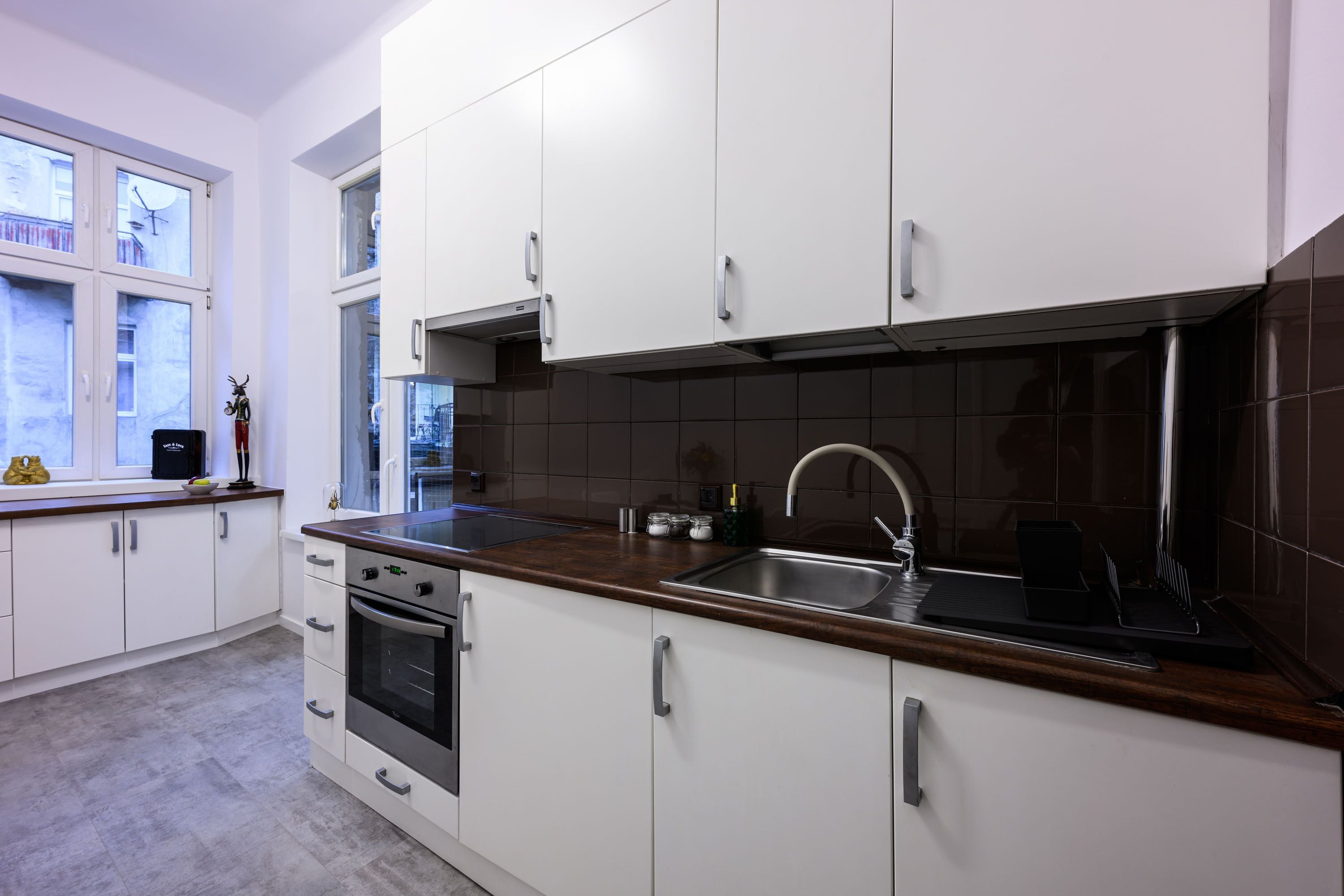 Una cocina moderna con armarios blancos, un lavamanos de acero inoxidable y un horno empotrado.