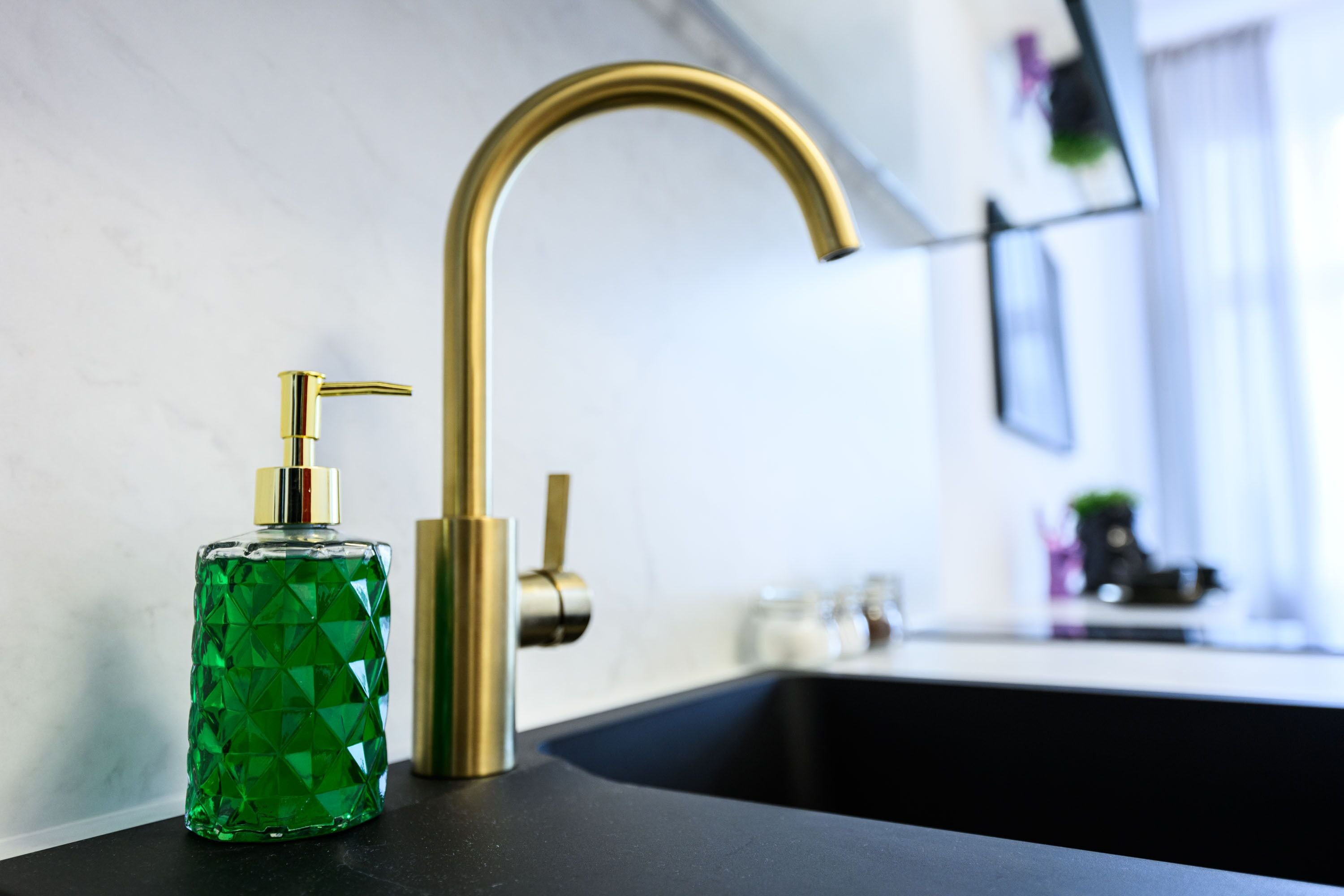 Une salle de bain avec un robinet doré, un distributeur de savon vert et un comptoir noir.