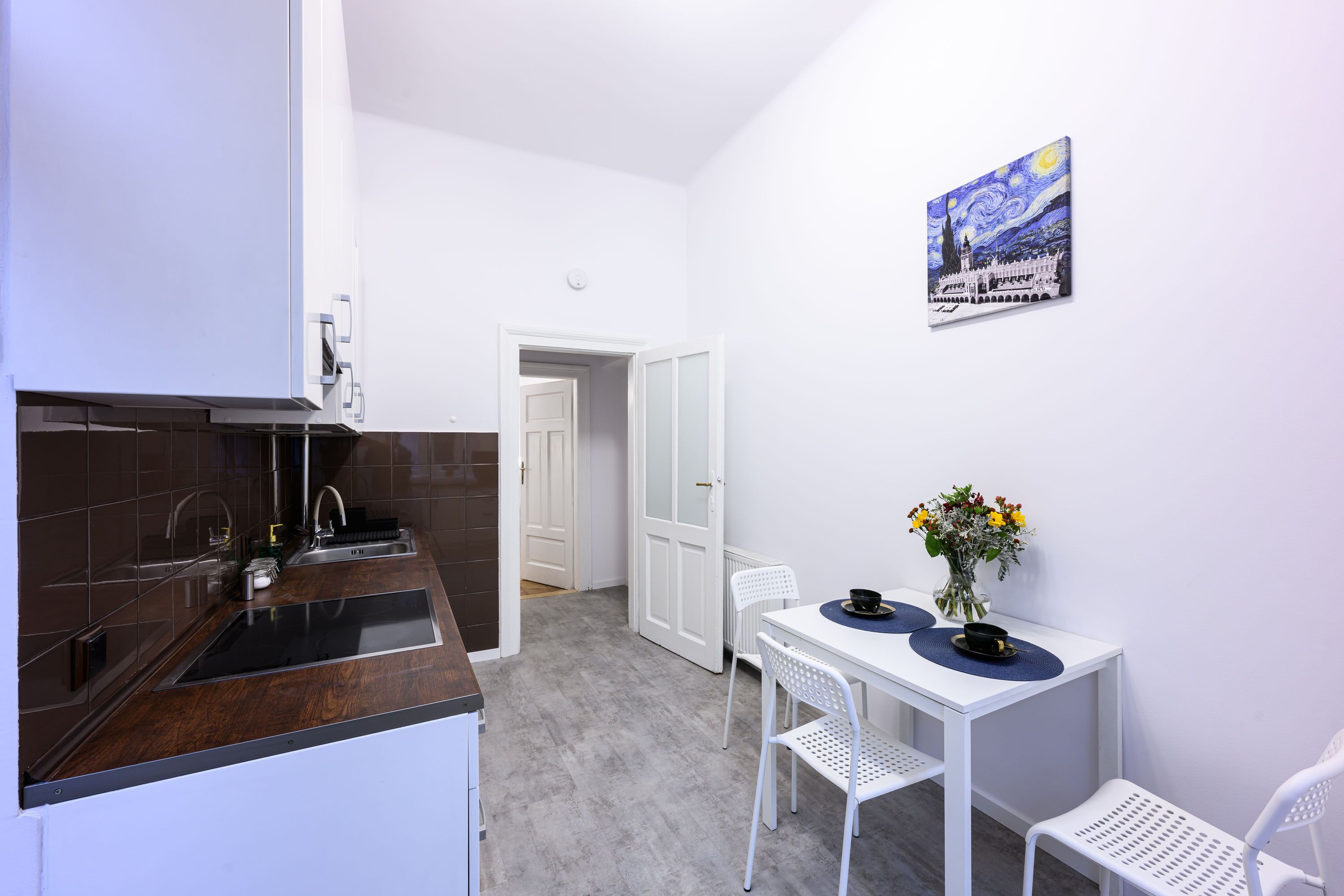 A modern kitchen with a dark wood countertop, white cabinetry, and a white dining area with two chairs and a table.