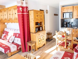 Una habitación acogedora con una cama, armarios de madera, una mesita y una zona de cocina con microondas.