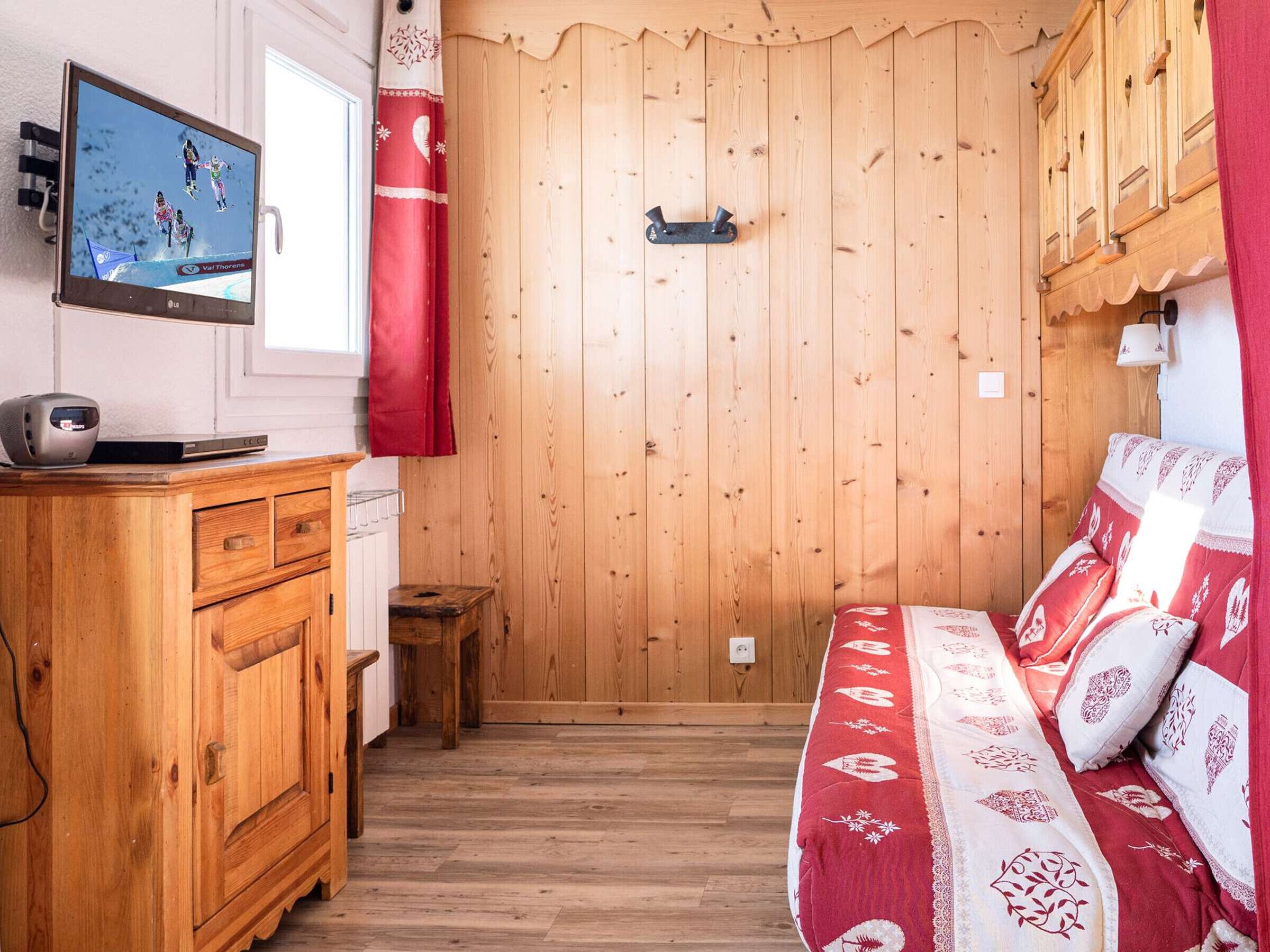 A wooden room with a bed, a wooden dresser, and a TV on the wall.
