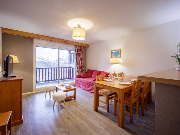 A cozy living room with a wooden dining table, a sofa, and a TV on a wooden cabinet. - Apartment for 8, Wi-Fi, parking - Peyragudes (Peyragudes)