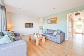 A living room with a sofa, a coffee table, and a dining table. There is a mirror on the wall and a door leading to another room.