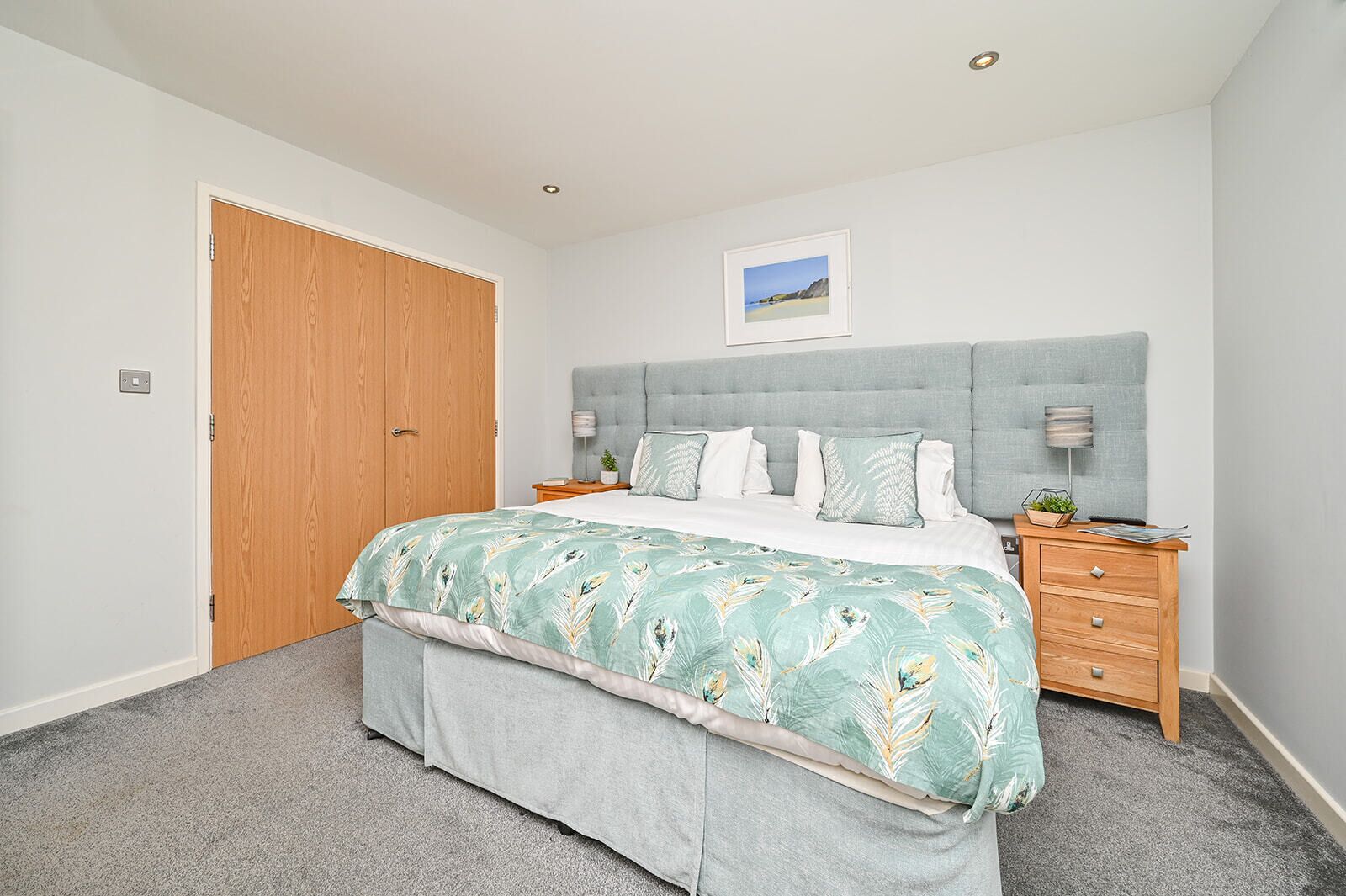 Une chambre à coucher avec un lit, une porte en bois, une table de chevet, une commode et un tableau encadré au mur.