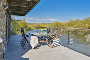 Une terrasse avec une table et des chaises donnant sur un plan d’eau, et un mur de briques sur un des côtés.