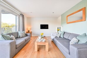 A modern living room with two grey sofas, a wooden coffee table, and a TV mounted on the wall.