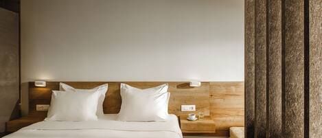 A hotel room with a wooden headboard, two white pillows, a bedside table with a cup and a glass, and a wooden nightstand.