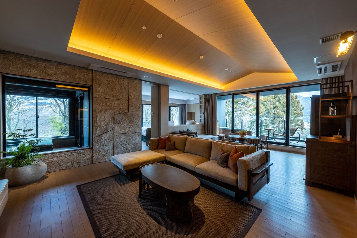A modern living room with a sectional sofa, a coffee table, and large windows offering a view of the outdoors.