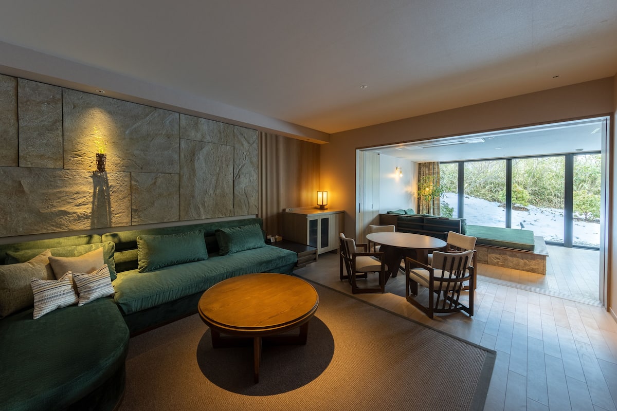 A modern living room with a green sofa, a round coffee table, and a dining area with chairs.