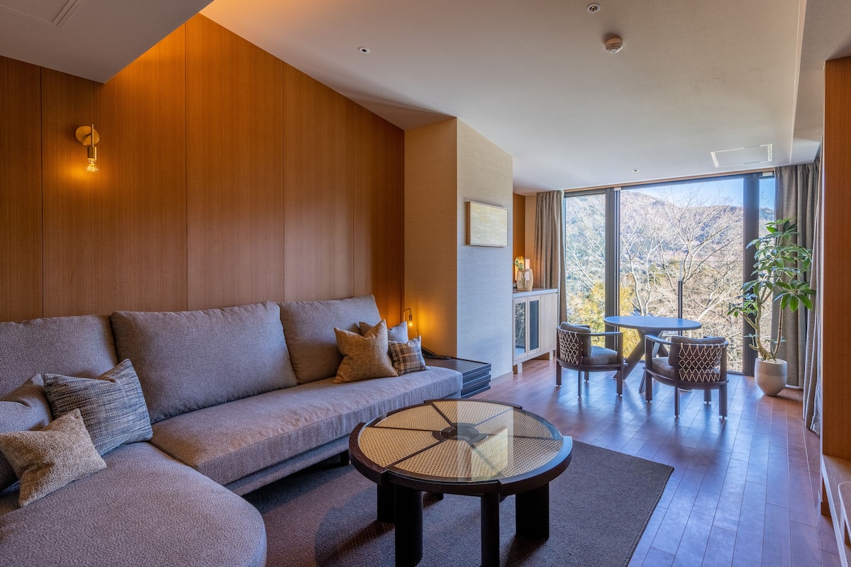 A modern living room with a sectional sofa, a glass coffee table, and a view of a mountainous landscape through large windows.