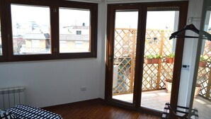 A room with a wooden floor, a bed, a radiator, and a sliding glass door leading to a balcony with a wooden lattice fence and potted plants. - Bright and well-connected penthouse (Roma)