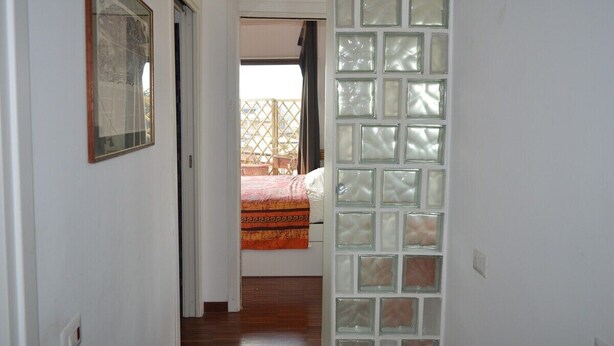 A hallway leading to a bedroom with a bed, a window with a view, and a door with frosted glass panels. - Bright and well-connected penthouse (Roma)